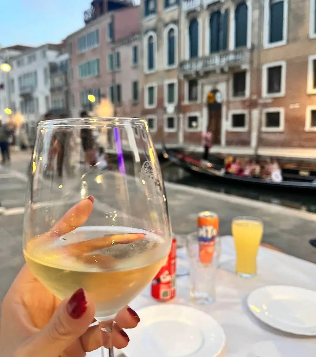 Glass of white wine on a canal-side terrace at sunset, gondola passing